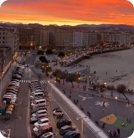 Vista de una zona de aparcamiento al anochecer, con luces encendidas y el cielo rojo