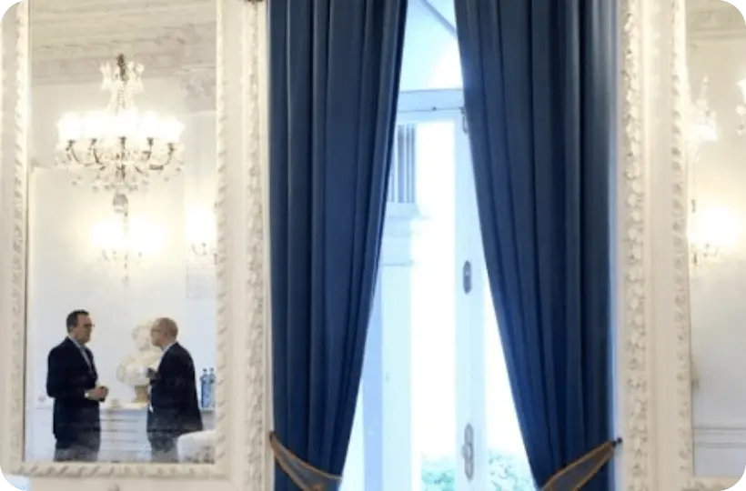 Sala con gran ventanal y espejos donde se reflejan un par de hombres con traje.